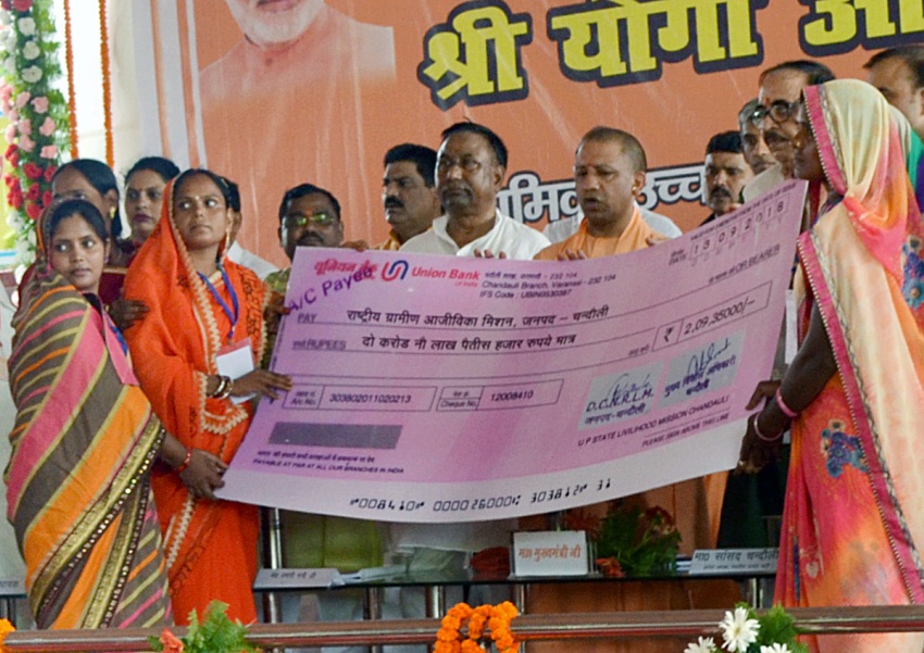 UPCM चन्दौली में जनकल्याणकारी योजनाओं के लाभार्थियों को चेक प्रदान करते हुए